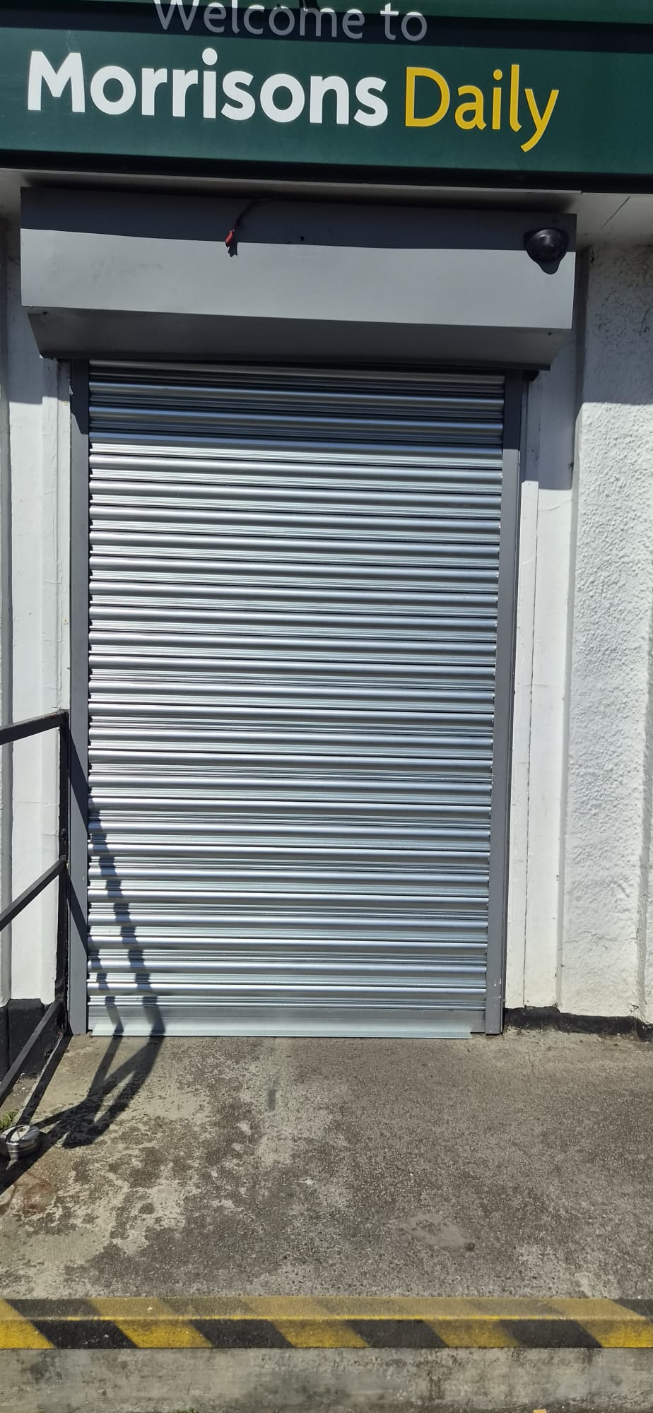 Newly installed silver roller shutter at Morrisons Daily storefront