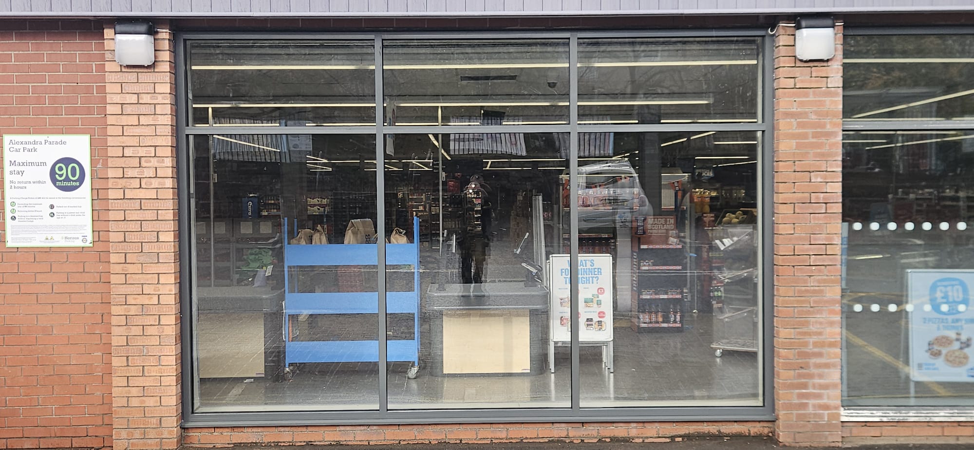Aluminium-framed full-bay shopfront glazing to convenience store, brick piers