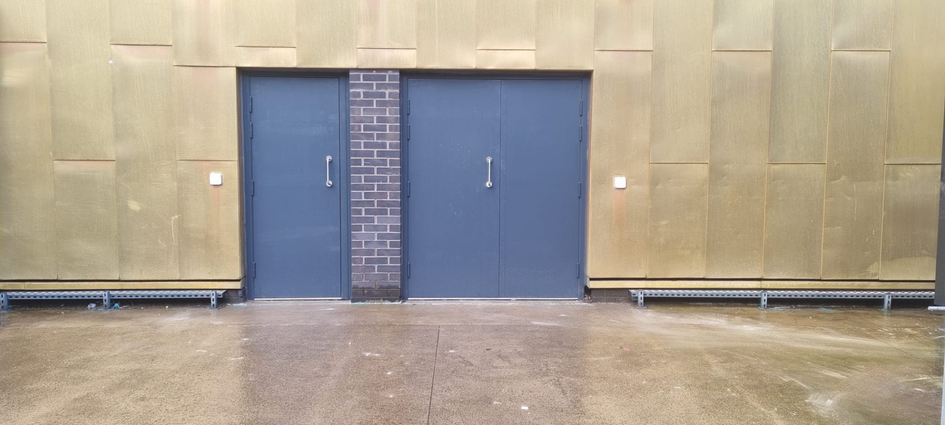Steel double fire doors, blue/grey finish, brick-faced industrial elevation
