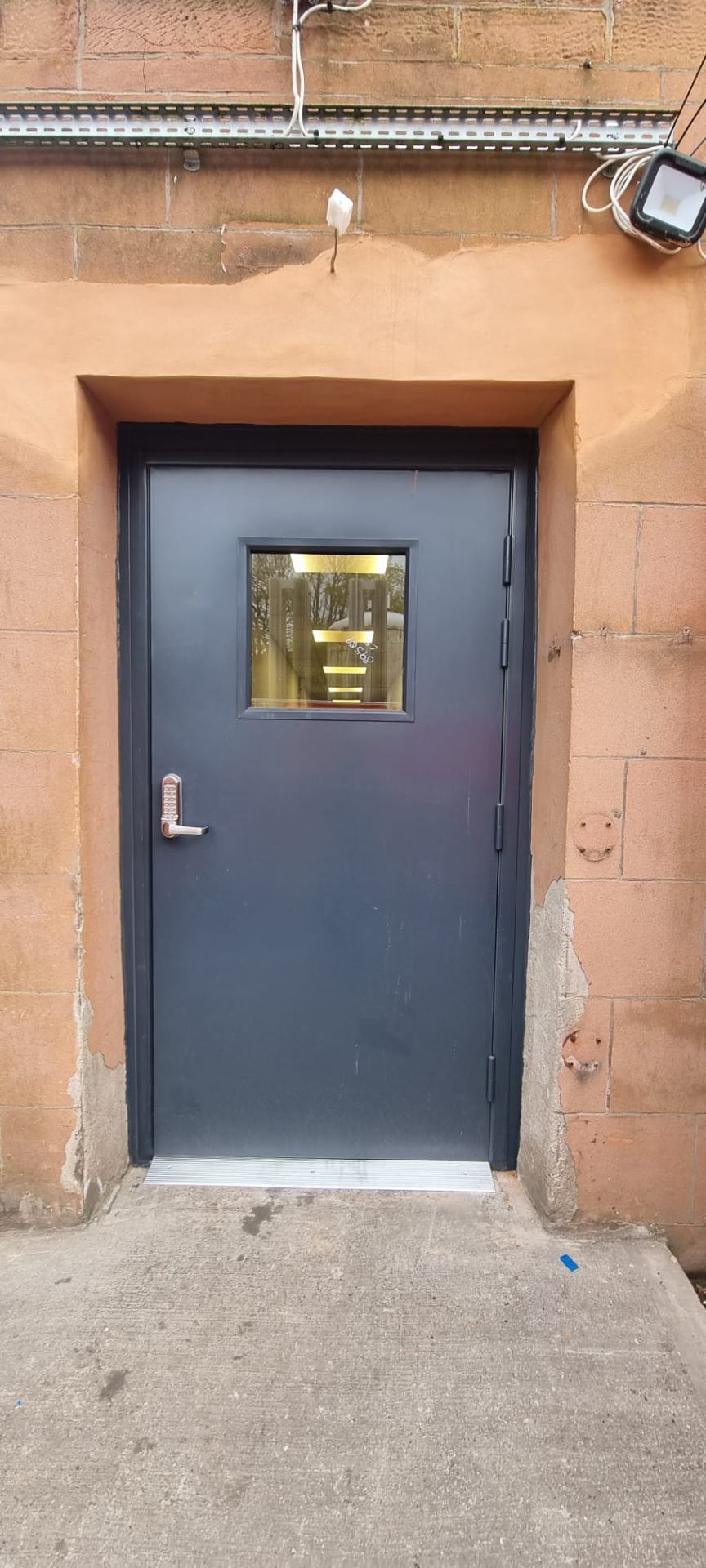 Steel security door with vision panel and digital code lock, sandstone reveal
