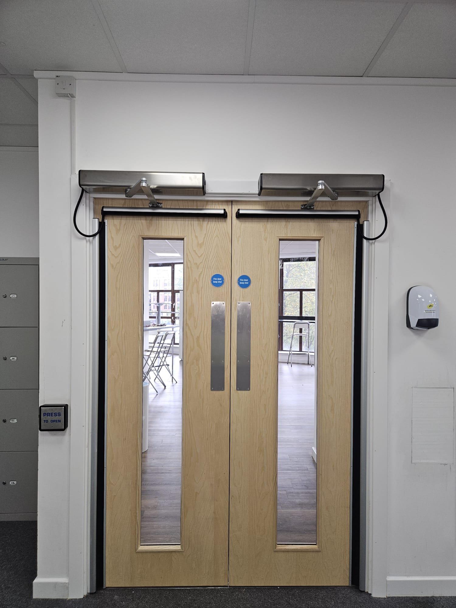 Oak fire-door pair with twin automatic swing operators and stainless push plates