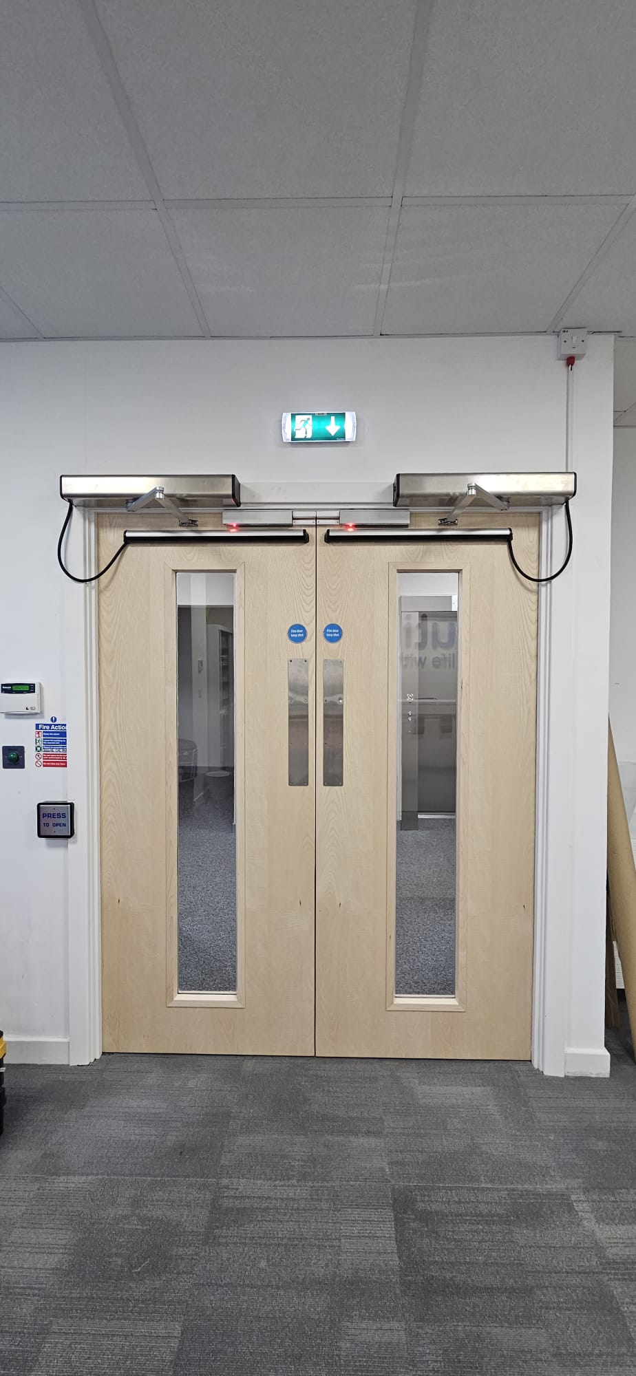 Oak fire-door pair with automatic operators and active-LED indicators in office foyer