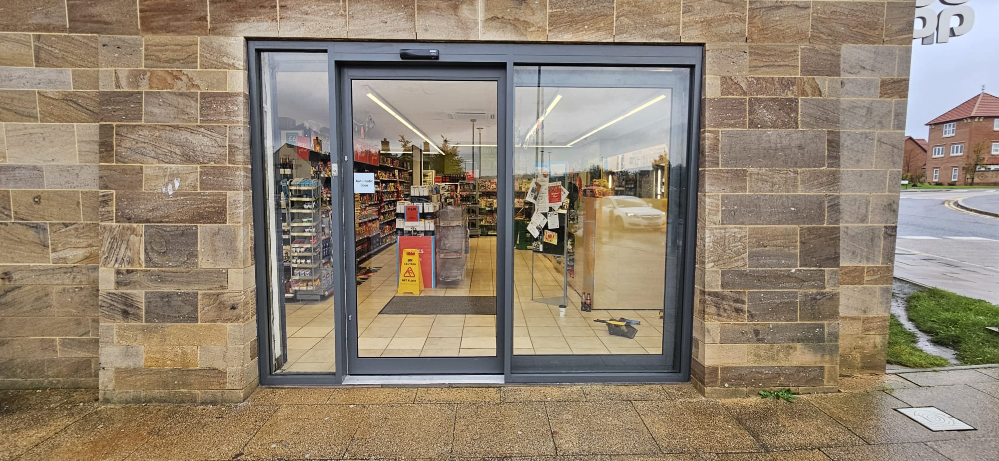 Aluminium-framed automatic sliding door at convenience store, sandstone elevation