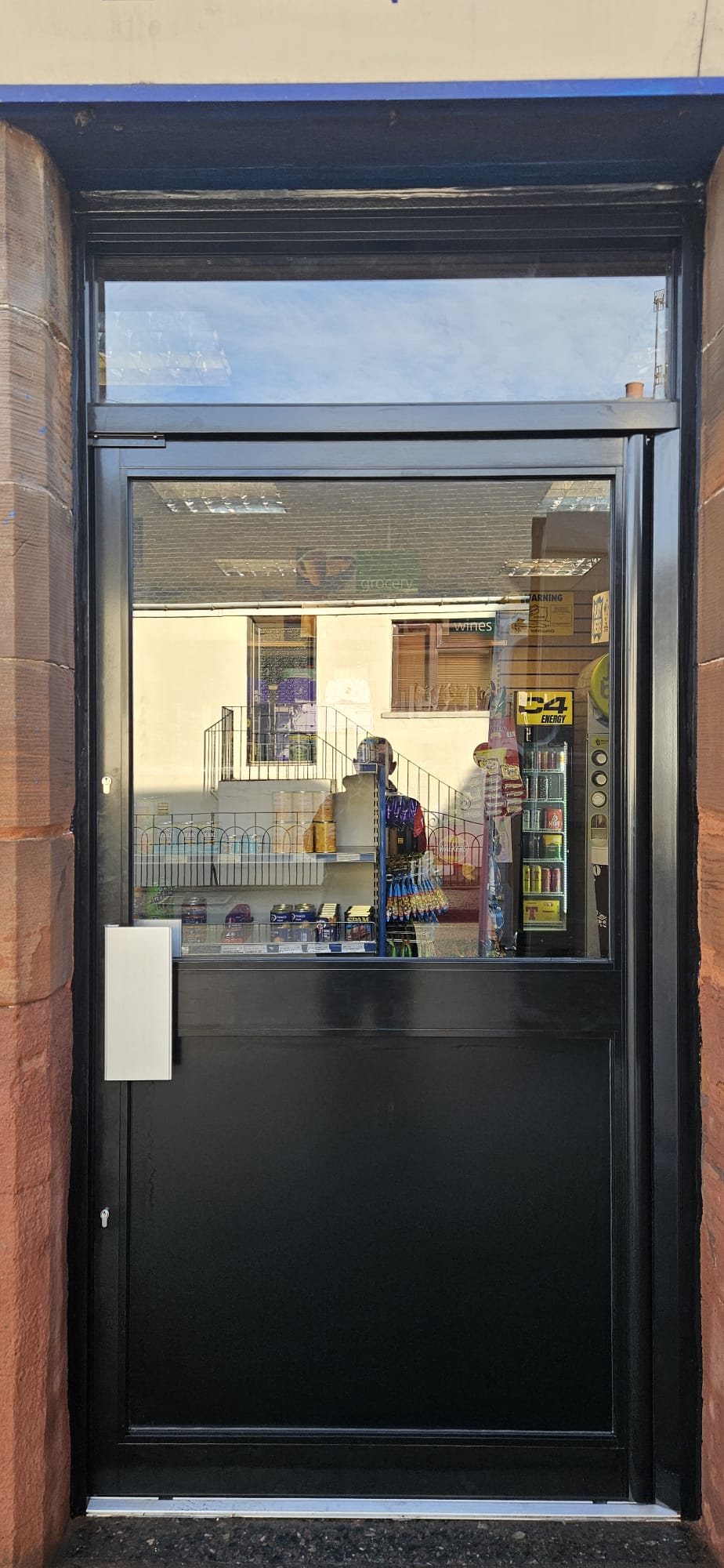 Half-glazed black aluminium entrance door at convenience store, sandstone surround