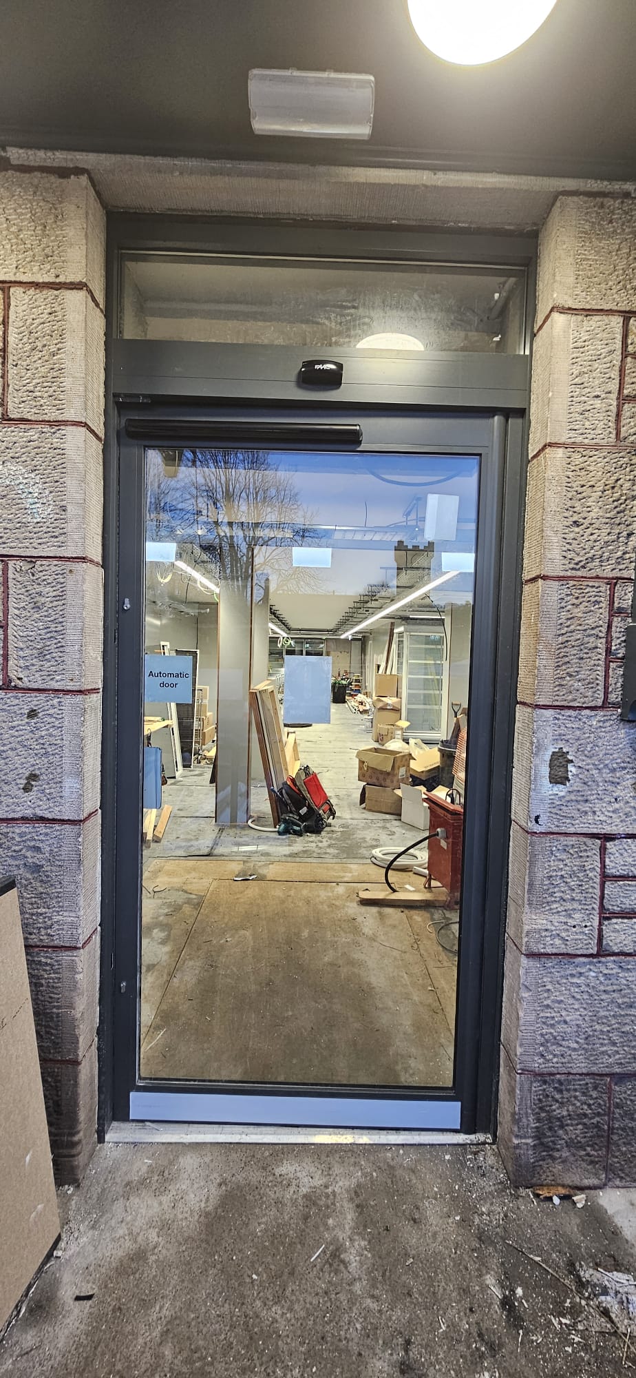Anthracite aluminium-framed automatic entrance door with FAAC operator, sandstone surround