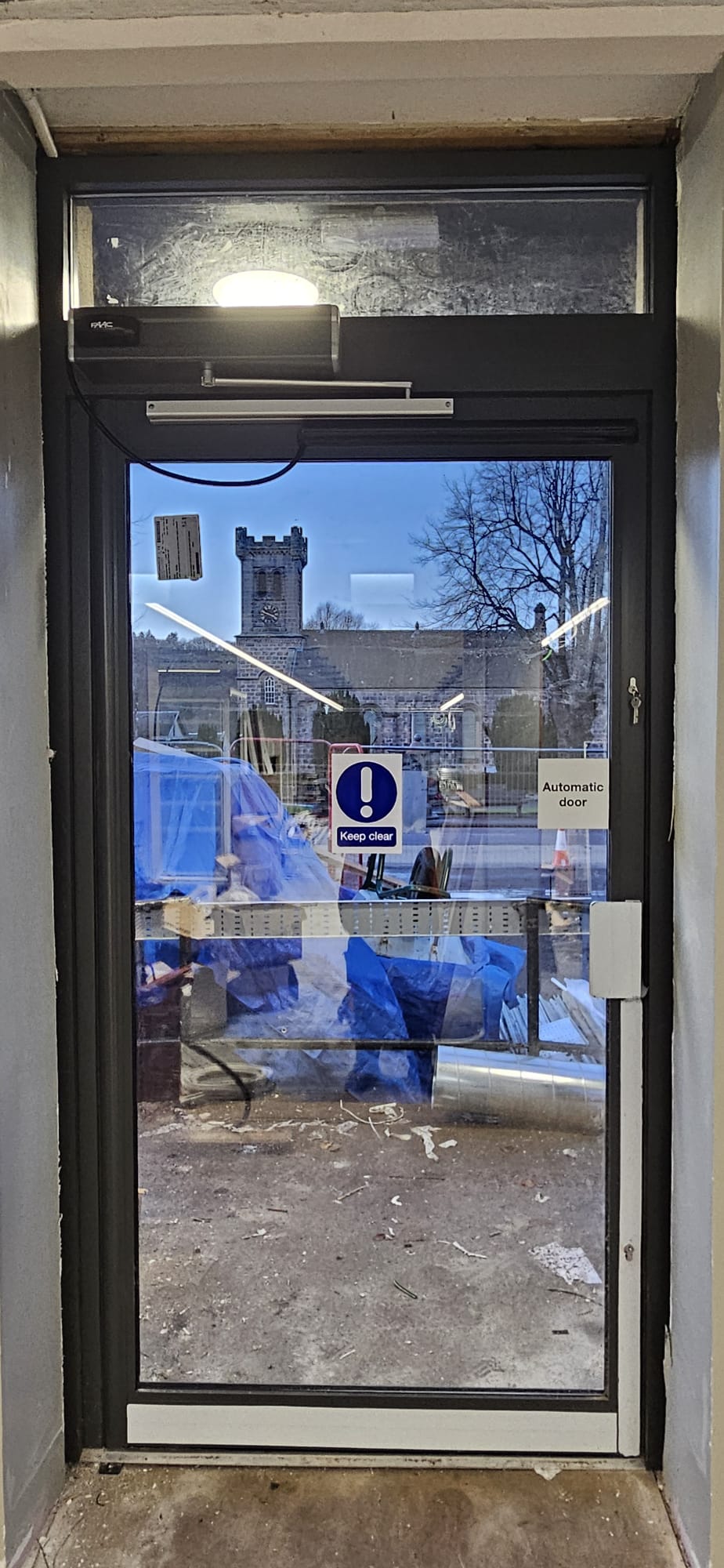 Aluminium-framed automatic entrance door with FAAC operator, church spire reflection