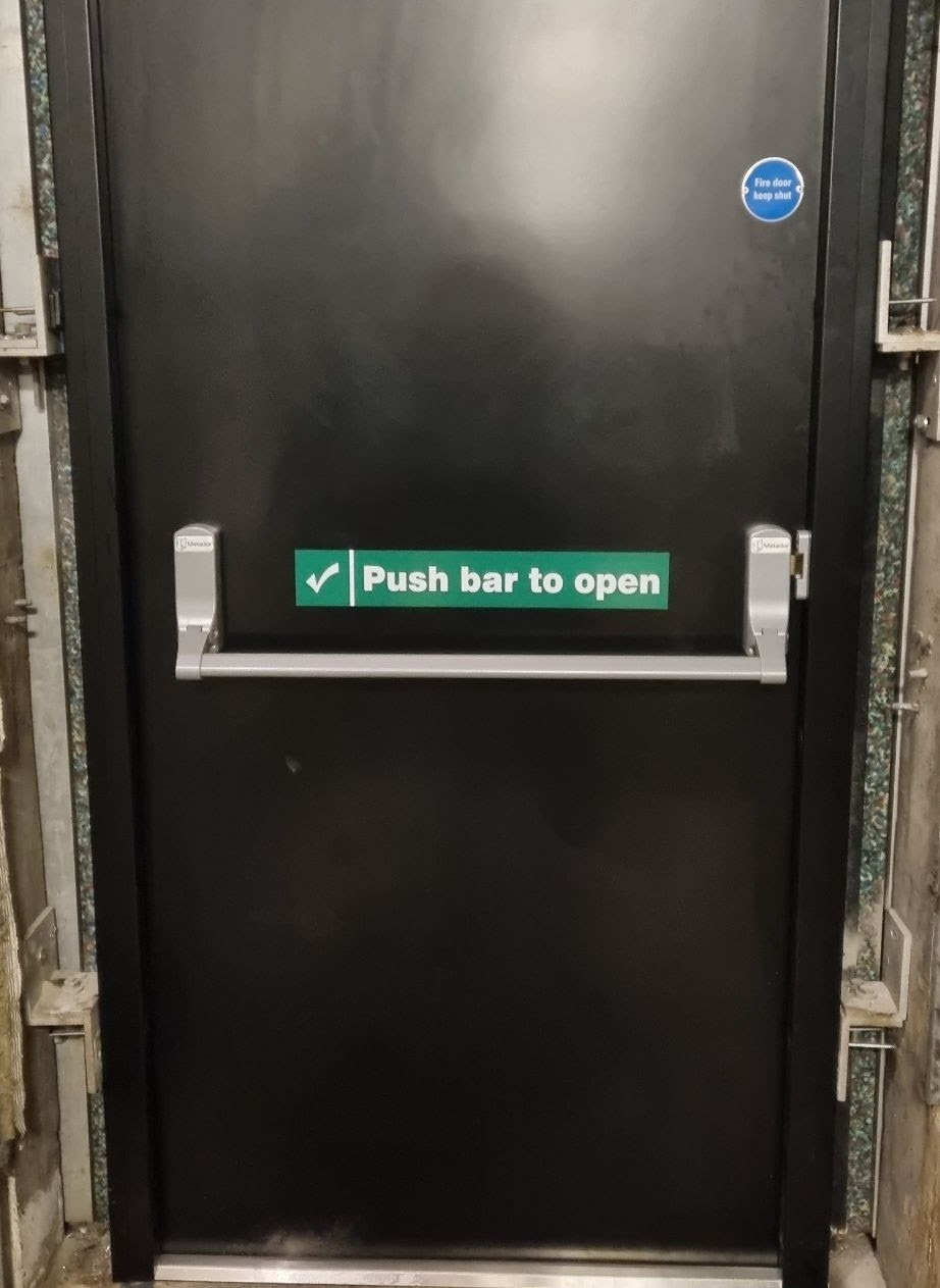 Single black steel fire door with push bar to open hardware and Fire Door Keep Shut signage
