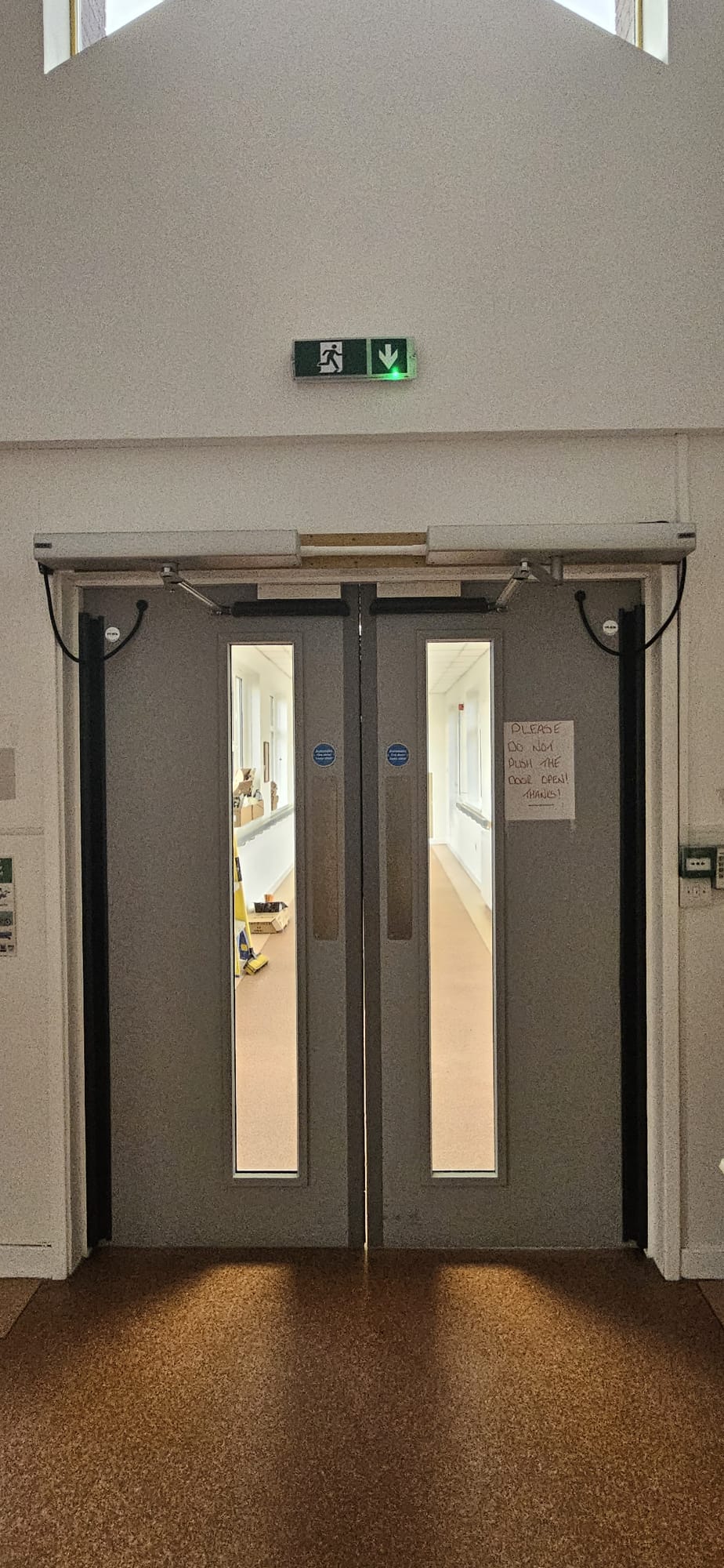 Pair of grey fire-rated swing doors with twin automatic operators in corridor