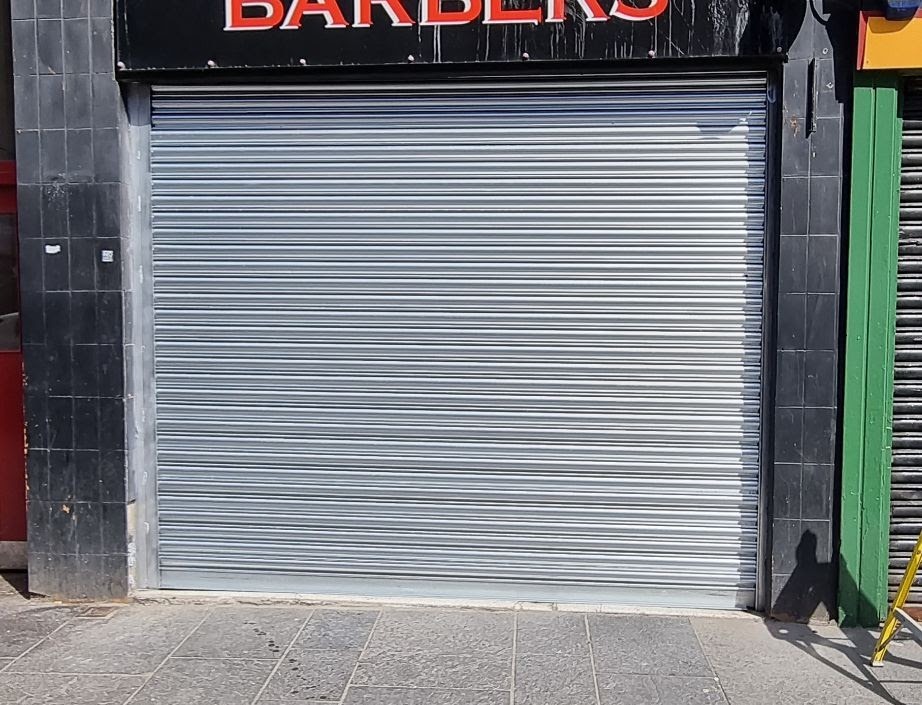 Newly installed silver security roller shutter to barber shop unit on high street
